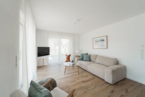 A modern living room with a sofa, a glass coffee table, and a television on a stand.