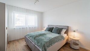 Ett sovrum med en säng, en sänglampa och ett fönster med tunna, genomskinliga gardiner.