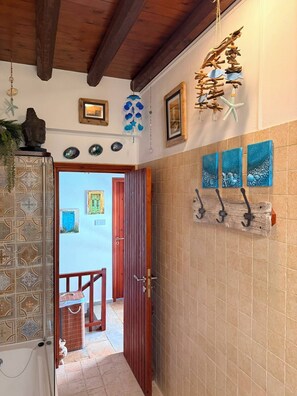 Un pasillo con techo de madera, una puerta que da a una habitación y un muro de azulejos con una obra de arte azul.