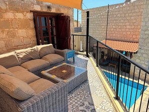 A balcony with a wicker sofa, a small table, and a pool.
