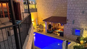 Zona de piscina con muros de piedra, mobiliario exterior y vistas al paisaje urbano.