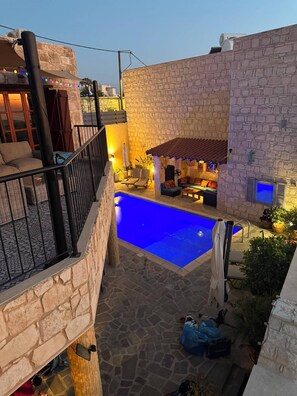 Zona de piscina con muros de piedra, mobiliario exterior y vistas al paisaje urbano.