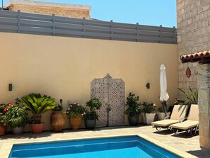 Una piscina con pared de azulejos, plantas en macetas y sillones de descanso.