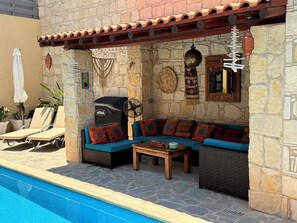 Ein Sitzbereich am Pool mit Steinmauer, Grill und Ventilator.