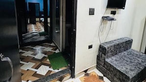 A hotel room with a patterned floor, a television mounted on the wall, and a small seating area. - Royal Guest House (Almora)