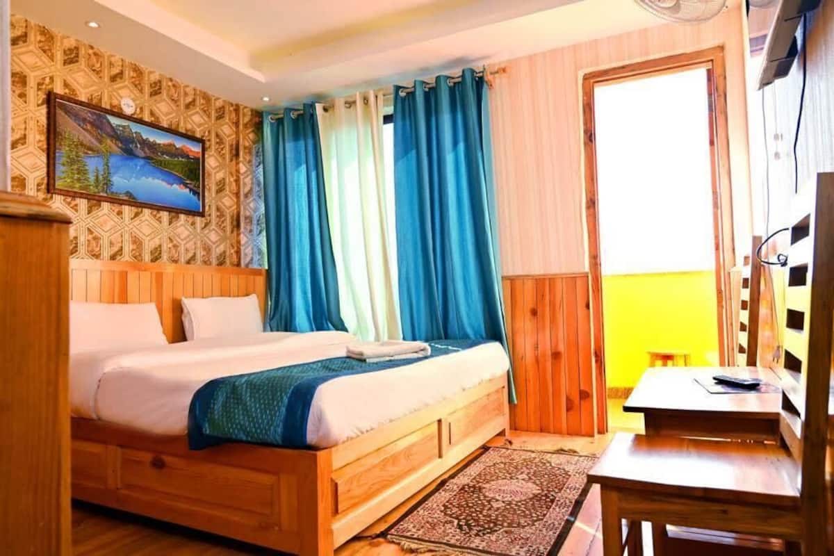 A wooden bed with a blue blanket, a wooden desk, and a painting on the wall.
