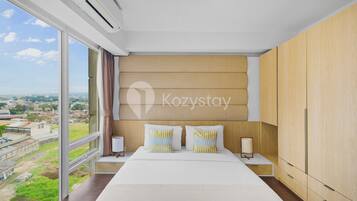 A modern hotel room with a large bed, wooden wardrobe, and a view of the city.
