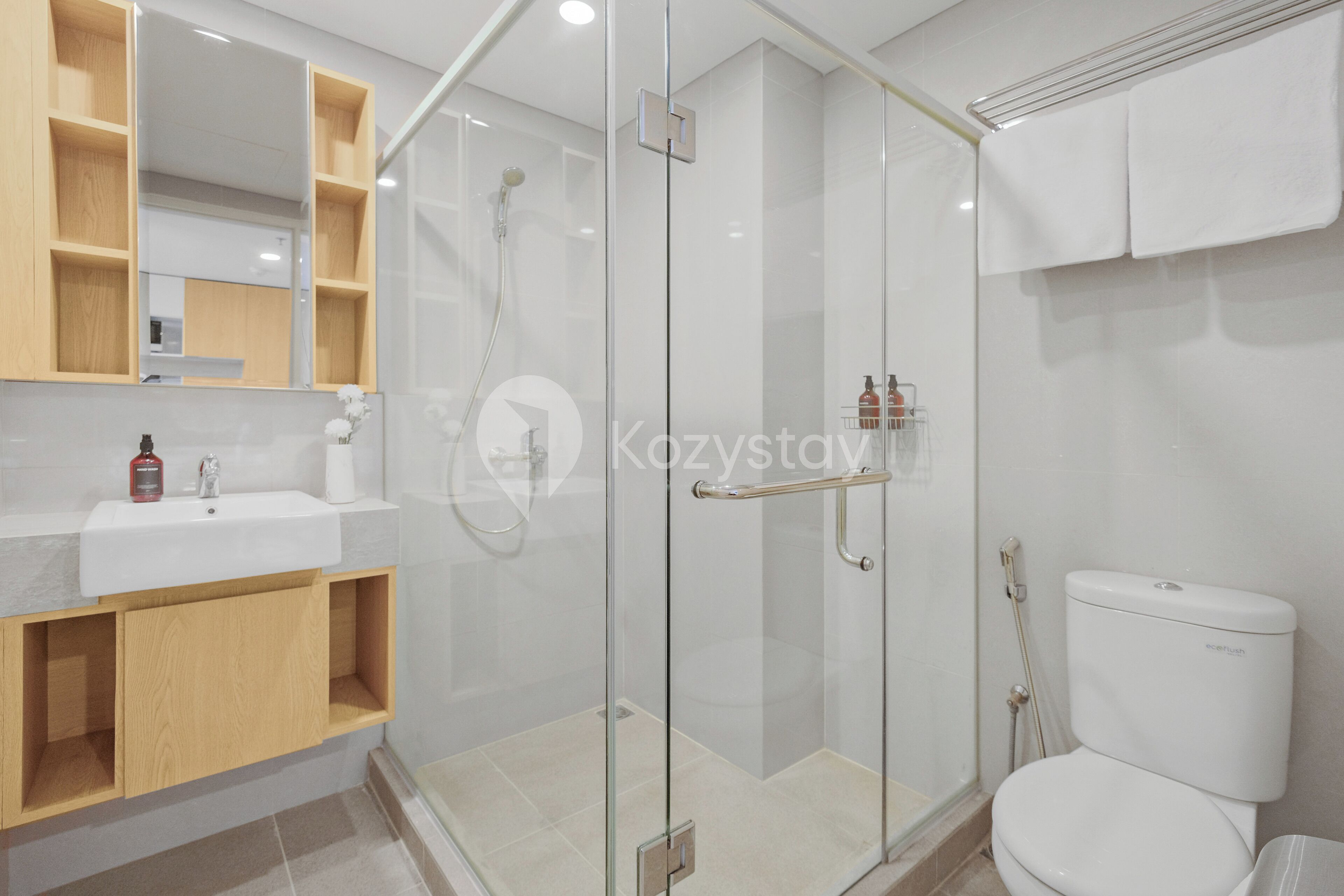 Un baño moderno con ducha de vidrio, lavamanos blanco y estanterías de madera.