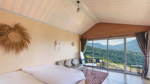 A bedroom with a bed, a sofa, a small table, and a view of the outdoors. - Fortune Glamping (Garung)