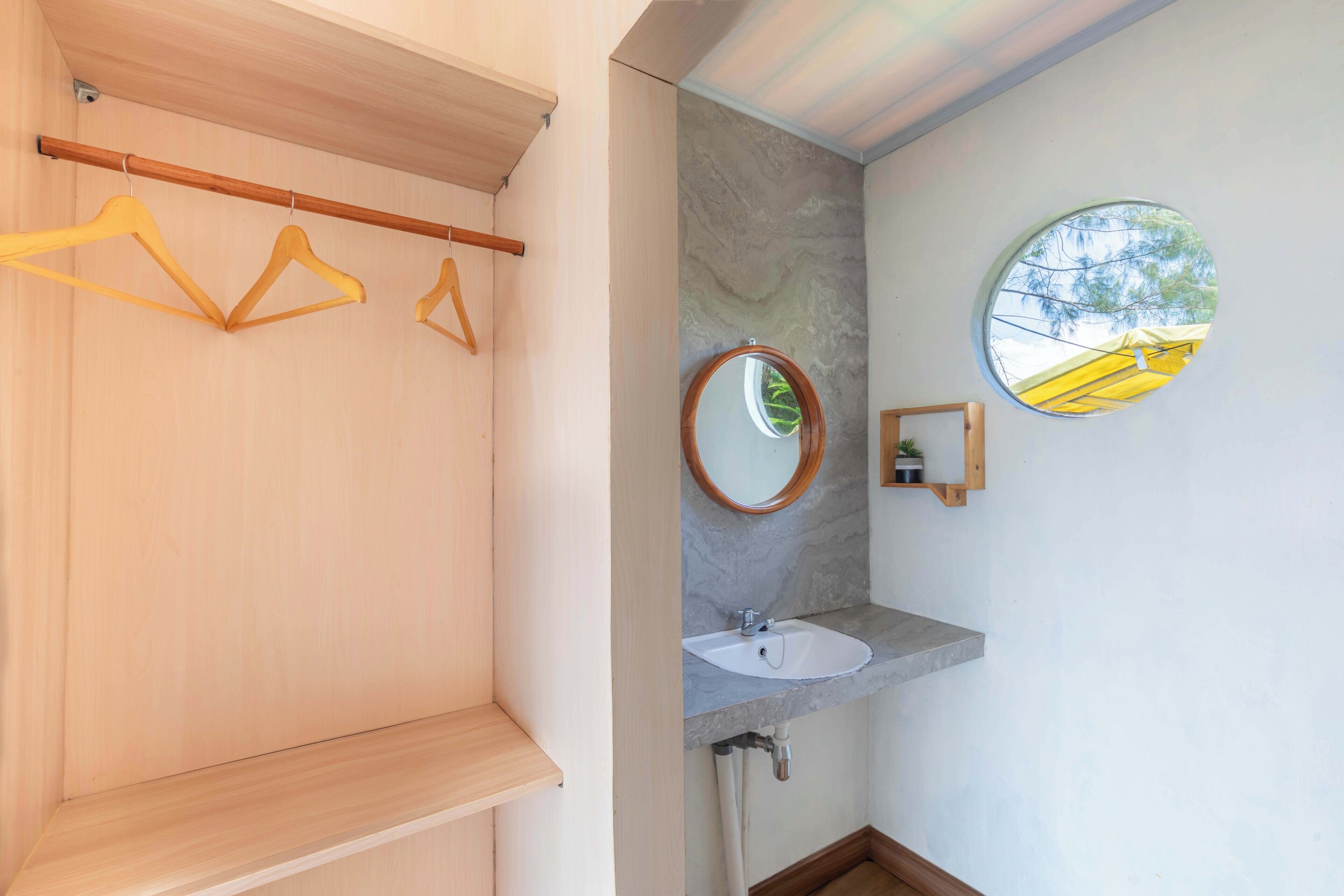Un baño con tocador de madera, un espejo redondo y una pequeña ventana.