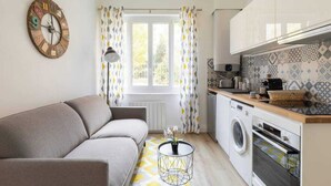 A compact living space with a sofa, a washing machine, and a kitchen area with a microwave and toaster.