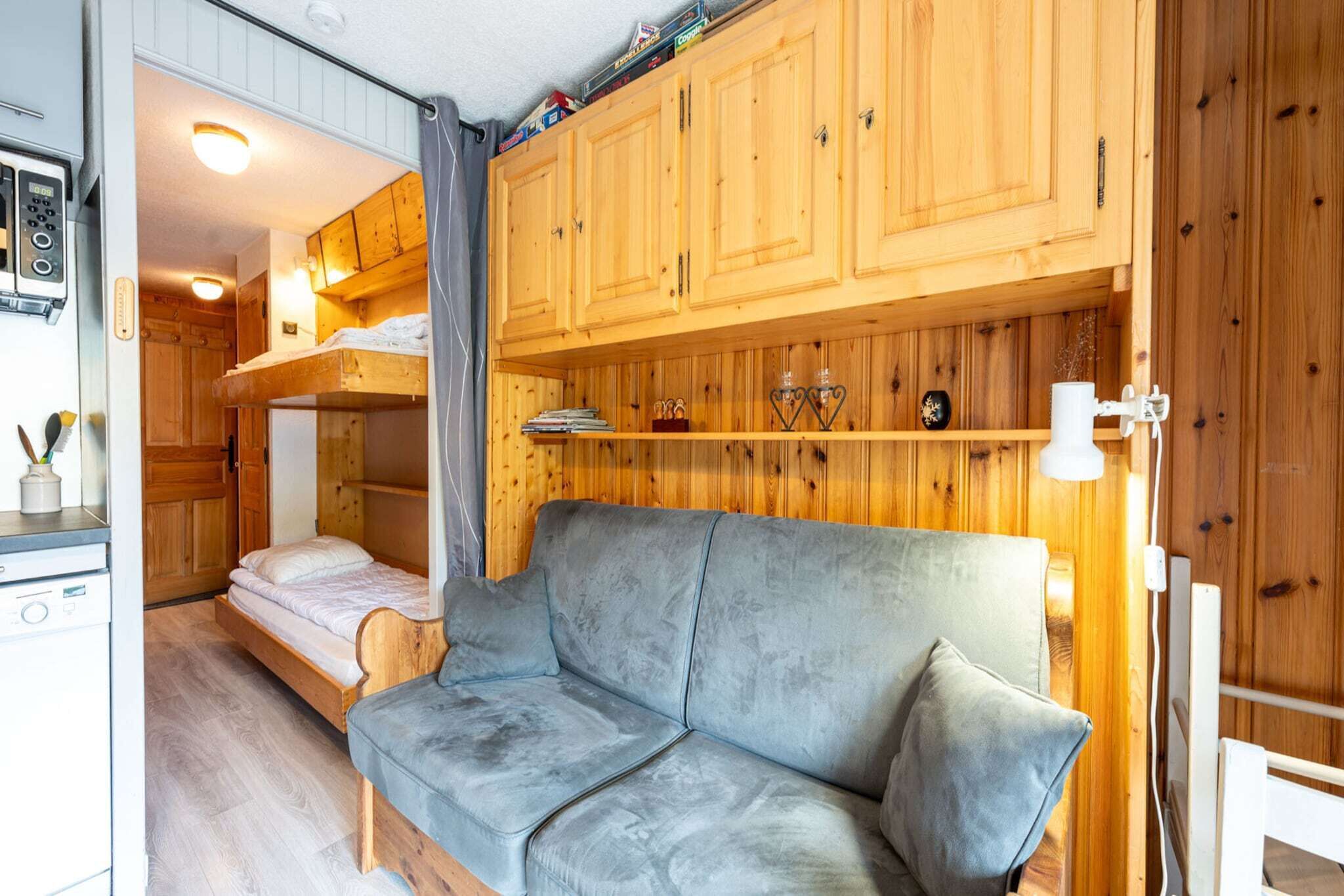 A compact room with a bunk bed, a sofa, wooden cabinets, and a small kitchenette.