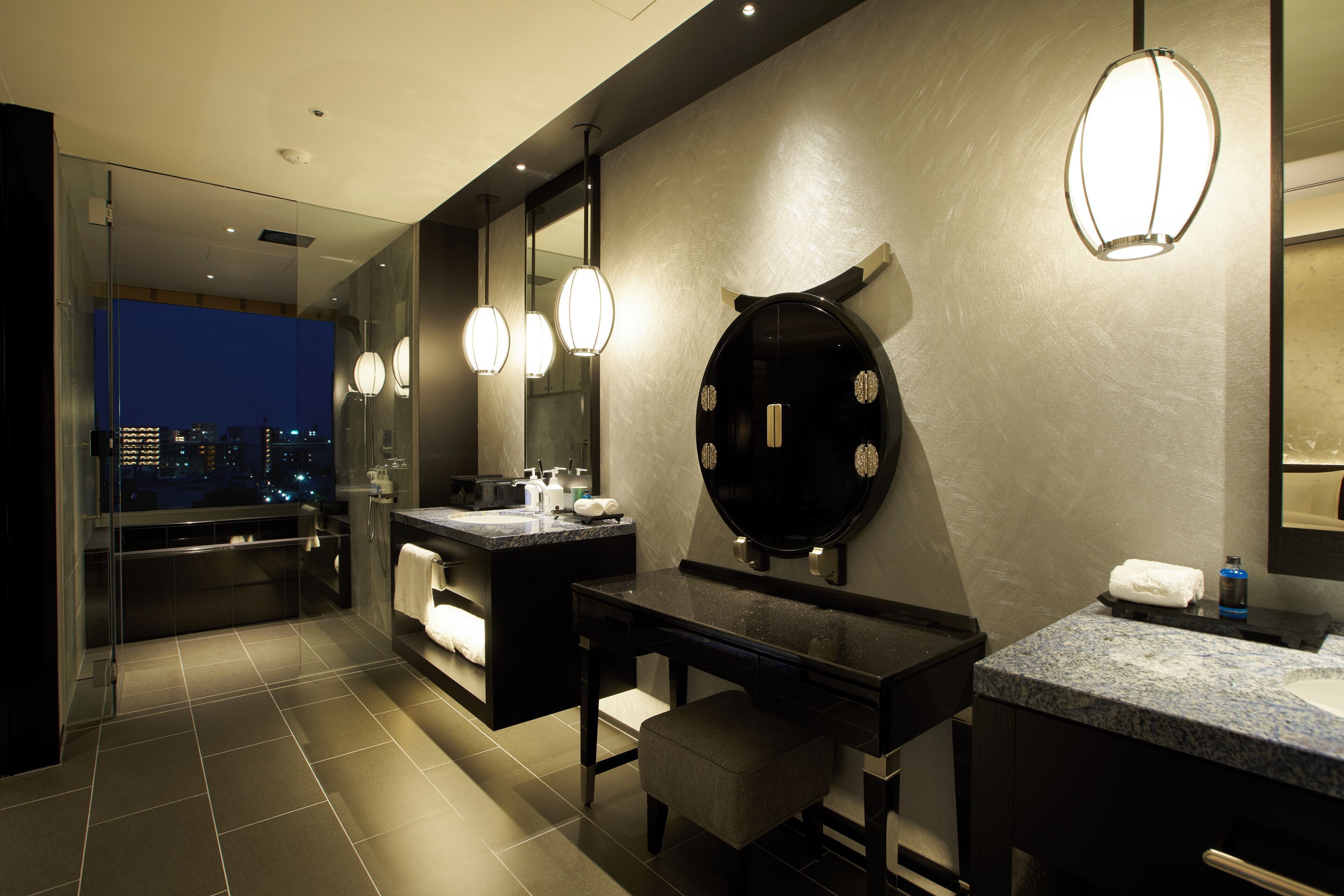 A modern bathroom with a large mirror, two sinks, a vanity, and a bench.