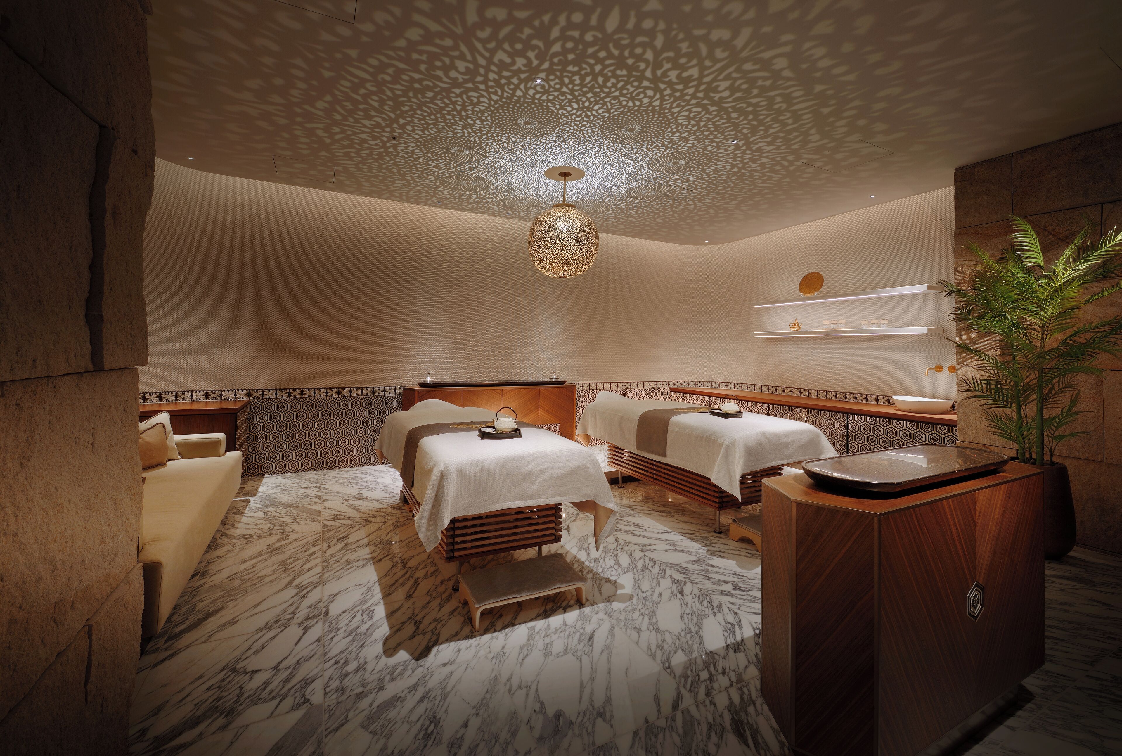Een spa-ruimte met twee massagetafels, een houten kast en een decoratief plafond.