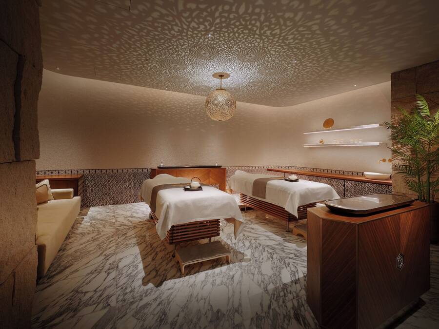 Een spa-ruimte met twee massagetafels, een houten kast en een decoratief plafond.
