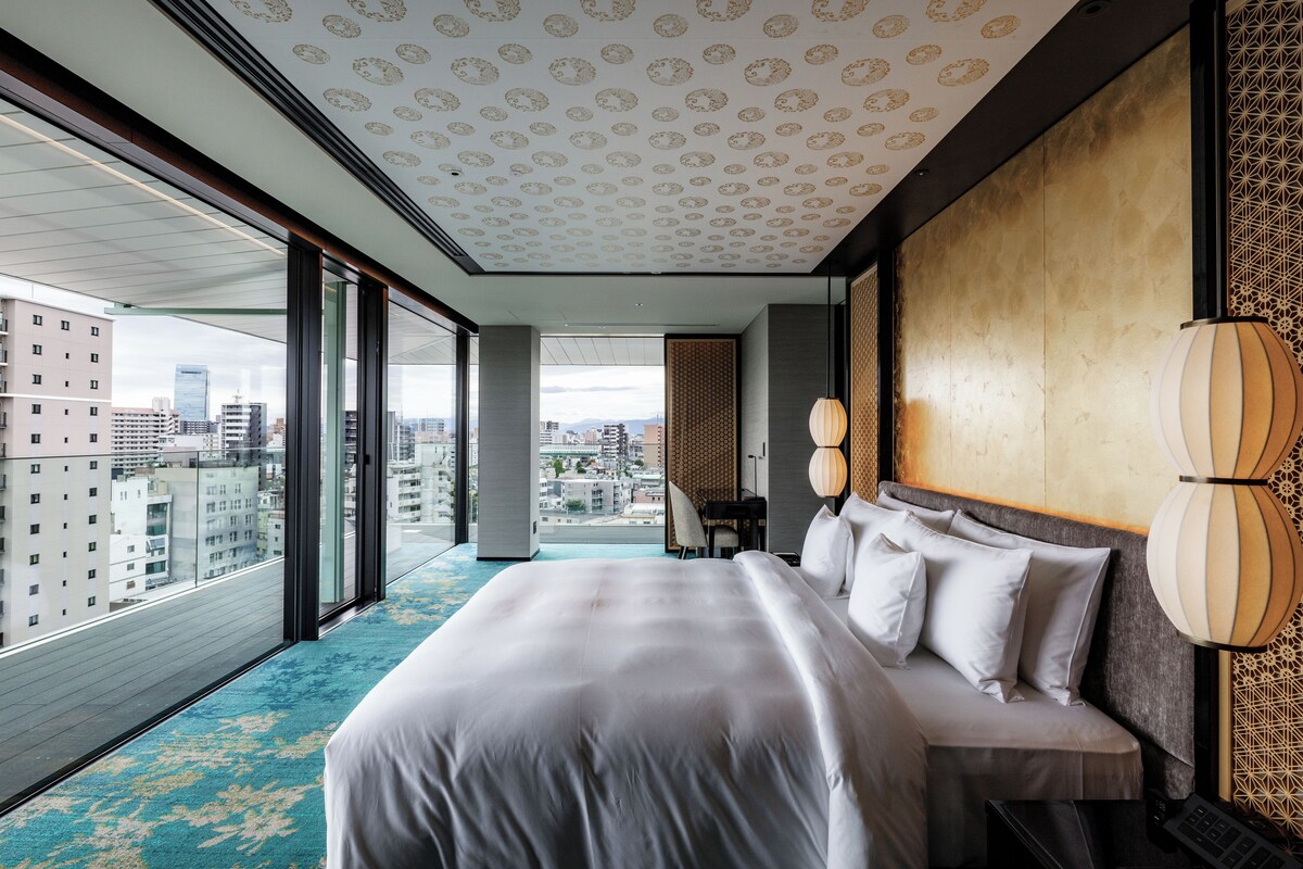A modern hotel room with a large bed, a desk, and a view of the city.