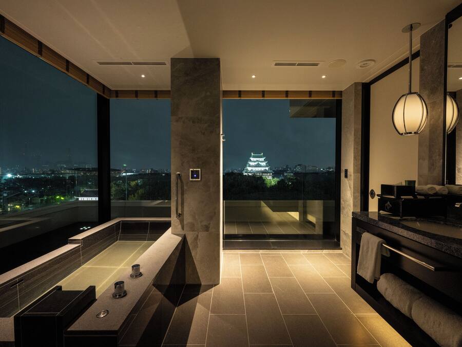 A modern bathroom with a large bathtub, a vanity with a mirror, and a view of a cityscape at night.