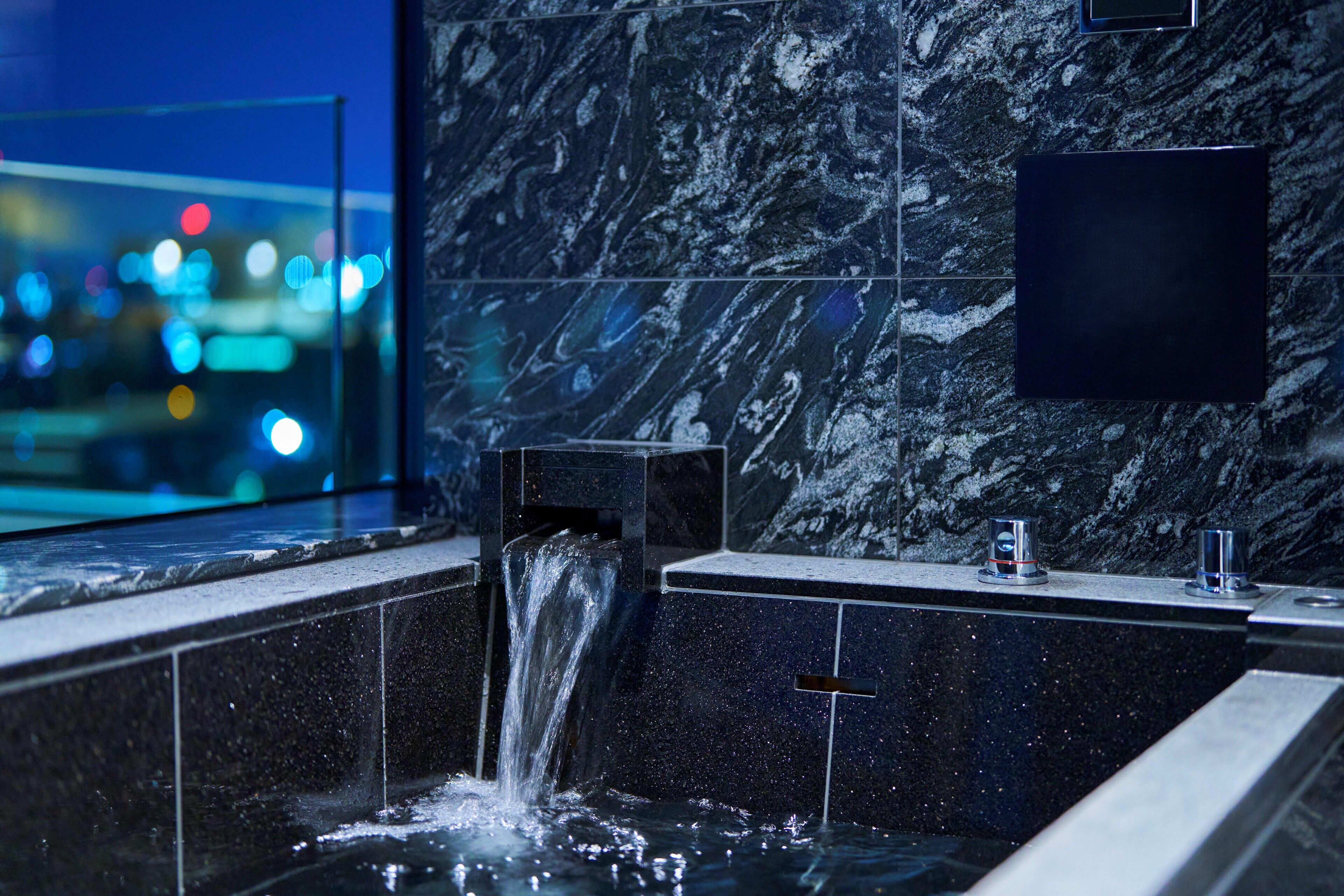 Un baño moderno con pared de mármol, ducha integrada y vistas a la ciudad de noche.