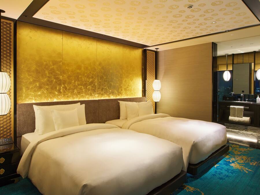 A hotel room with two beds, a large mirror, a bathroom with a sink and towel rack, and a patterned wall.
