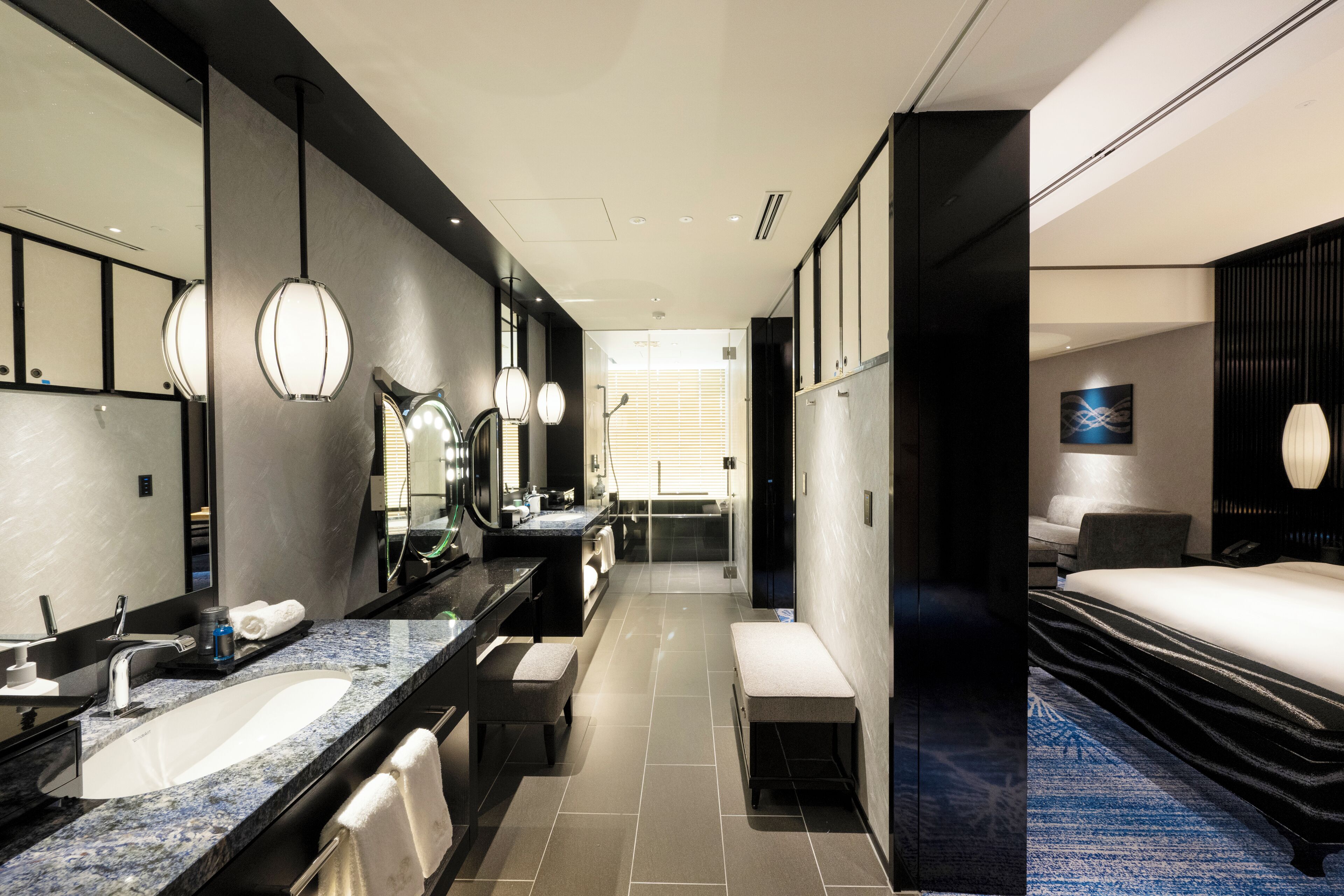 A modern hotel bathroom with a large sink, mirror, and bench.