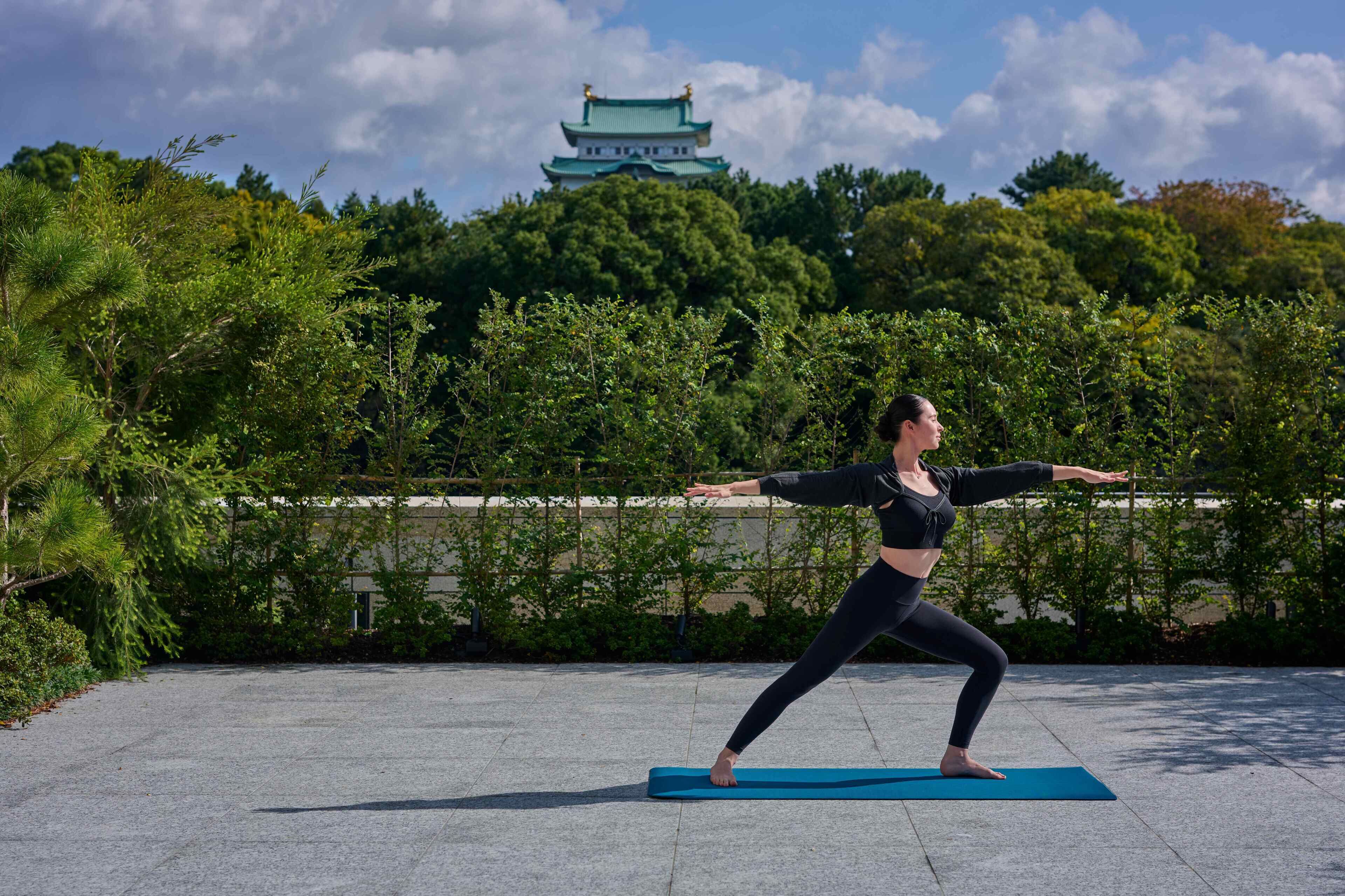 A person performing a yoga pose on a mat with a traditional building in the background.