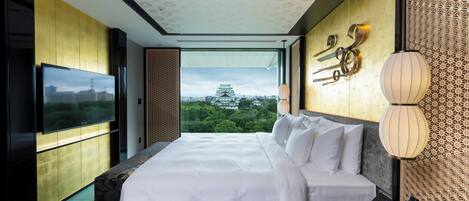 A modern hotel room with a large bed, a flat-screen TV, and a view of a traditional building.