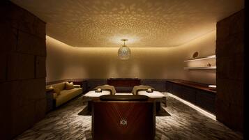A luxurious bathroom with a marble floor, a wooden vanity, a freestanding bathtub, and a beige sofa.