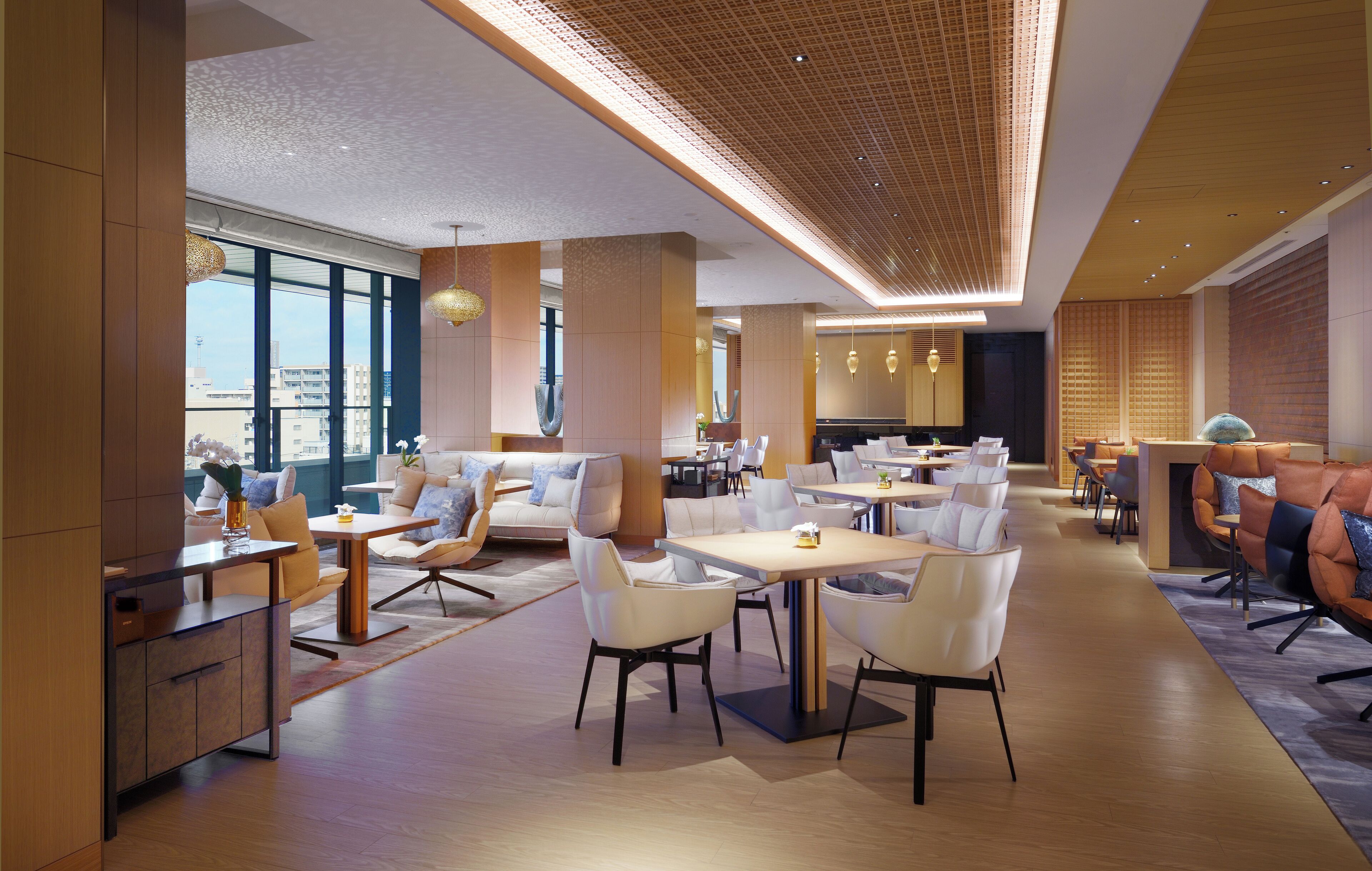 Eine moderne Hotelhalle mit großzügiger Sitzecke, großen Fenstern und einer hohen Decke mit Musterdesign.