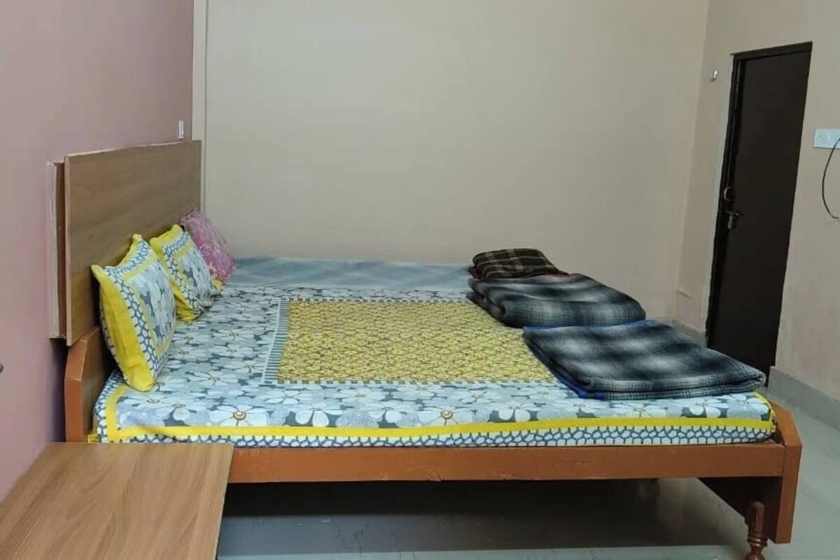 A single bed with a wooden headboard, a patterned bedspread, and a yellow mat.