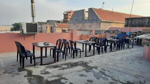 A rooftop terrace with tables and chairs, air conditioning units, and a view of surrounding buildings. - Sankatha Guest House (VARANASI)