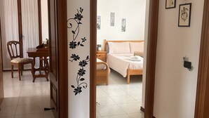 Una habitación con una cama, una silla y una mesa. Hay una puerta que da a otra habitación.