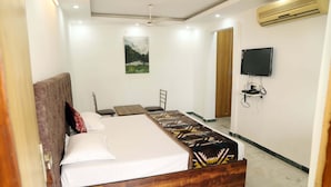 Quarto com cama, televisão fixada na parede e ventoinha no teto.