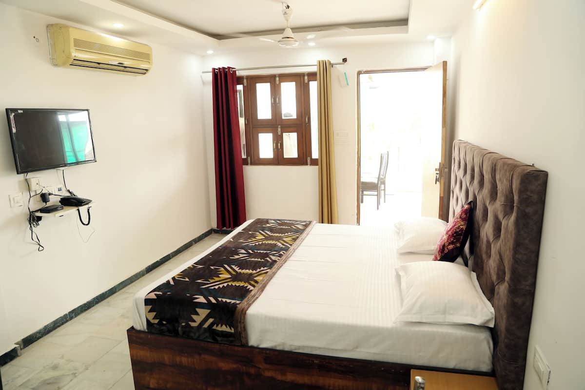Un dormitorio con cama, televisión, aire acondicionado y ventana con cortinas.