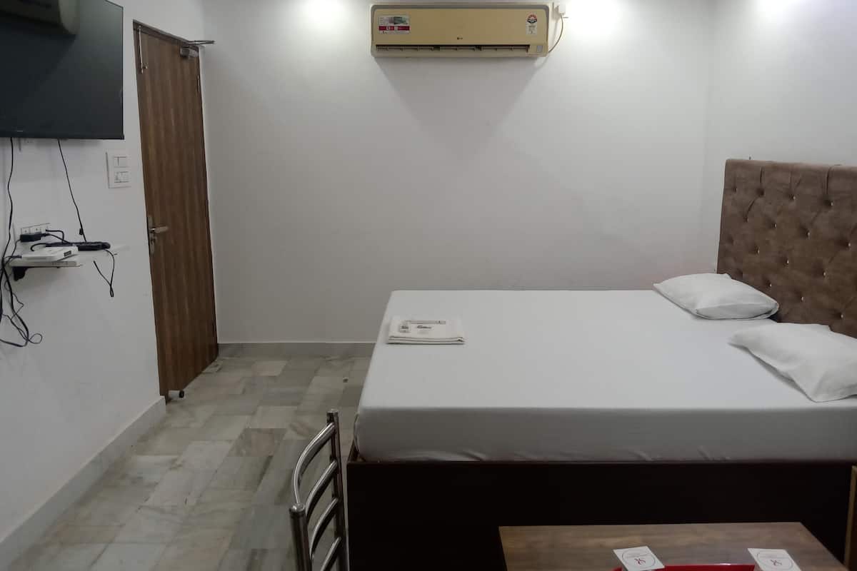 Un dormitorio con cama, televisor montado en la pared, aire acondicionado y una puerta de madera.