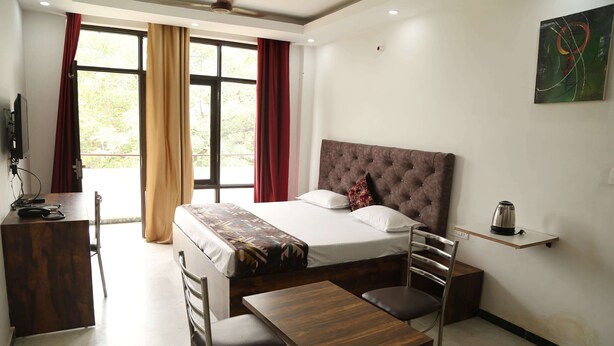 Quarto de hotel com uma cama, escrivaninha, cadeira, mesa e janela com cortinas.