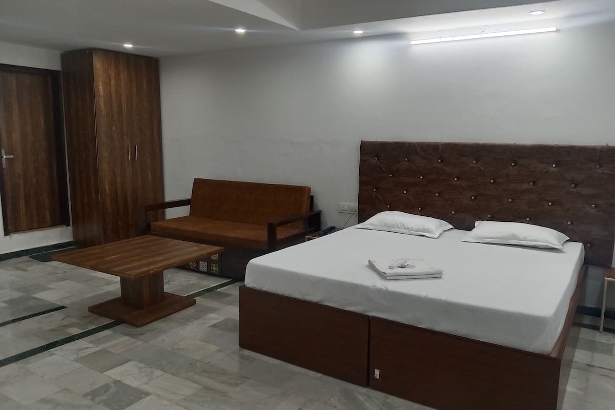 Una habitación de hotel con una cama grande, un banco de madera, un armario y una silla.