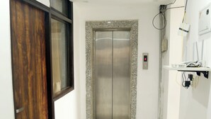 Um corredor com piso de mármore, porta de madeira e um elevador moderno.