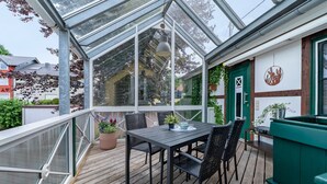 Ein Wintergarten mit Tisch, Stühlen, einer Hängelampe und einem grünen Pflanzgefäß.