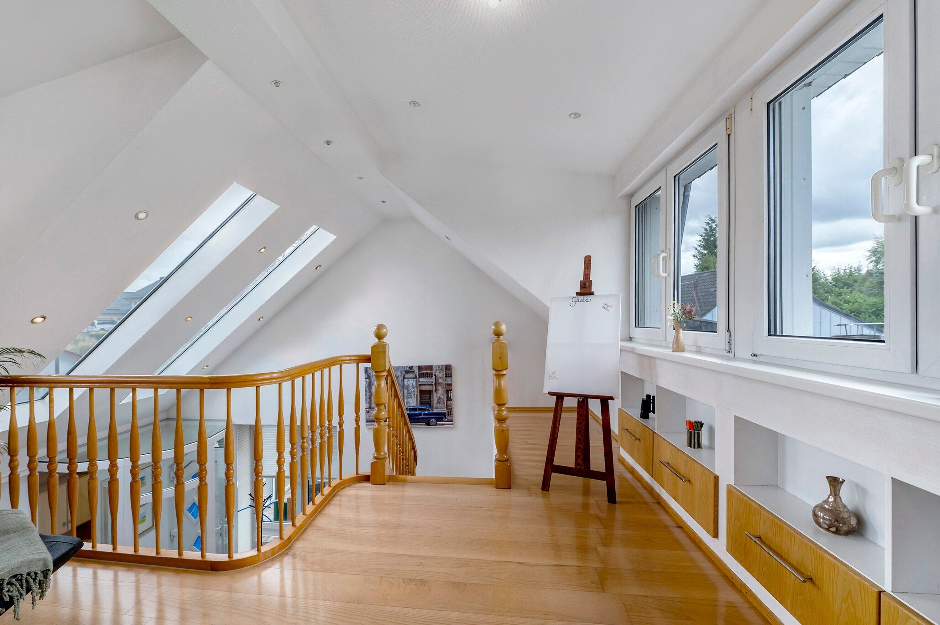 Ein geräumiges Schlafzimmer im Loft-Stil mit schrägem Dach, Dachfenstern, einer Holztreppe und einem großen Fenster mit Blick ins Freie.