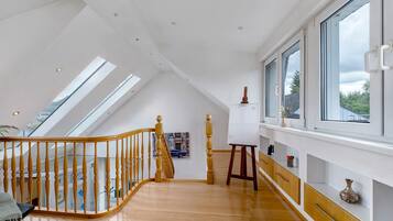 Ein geräumiges Schlafzimmer im Loft-Stil mit schrägem Dach, Dachfenstern, einer Holztreppe und einem großen Fenster mit Blick ins Freie.