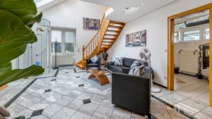 Ein großzügiger Wohnbereich mit Treppe, einer Sofagarnitur, einem Couchtisch und einer großen Pflanze.