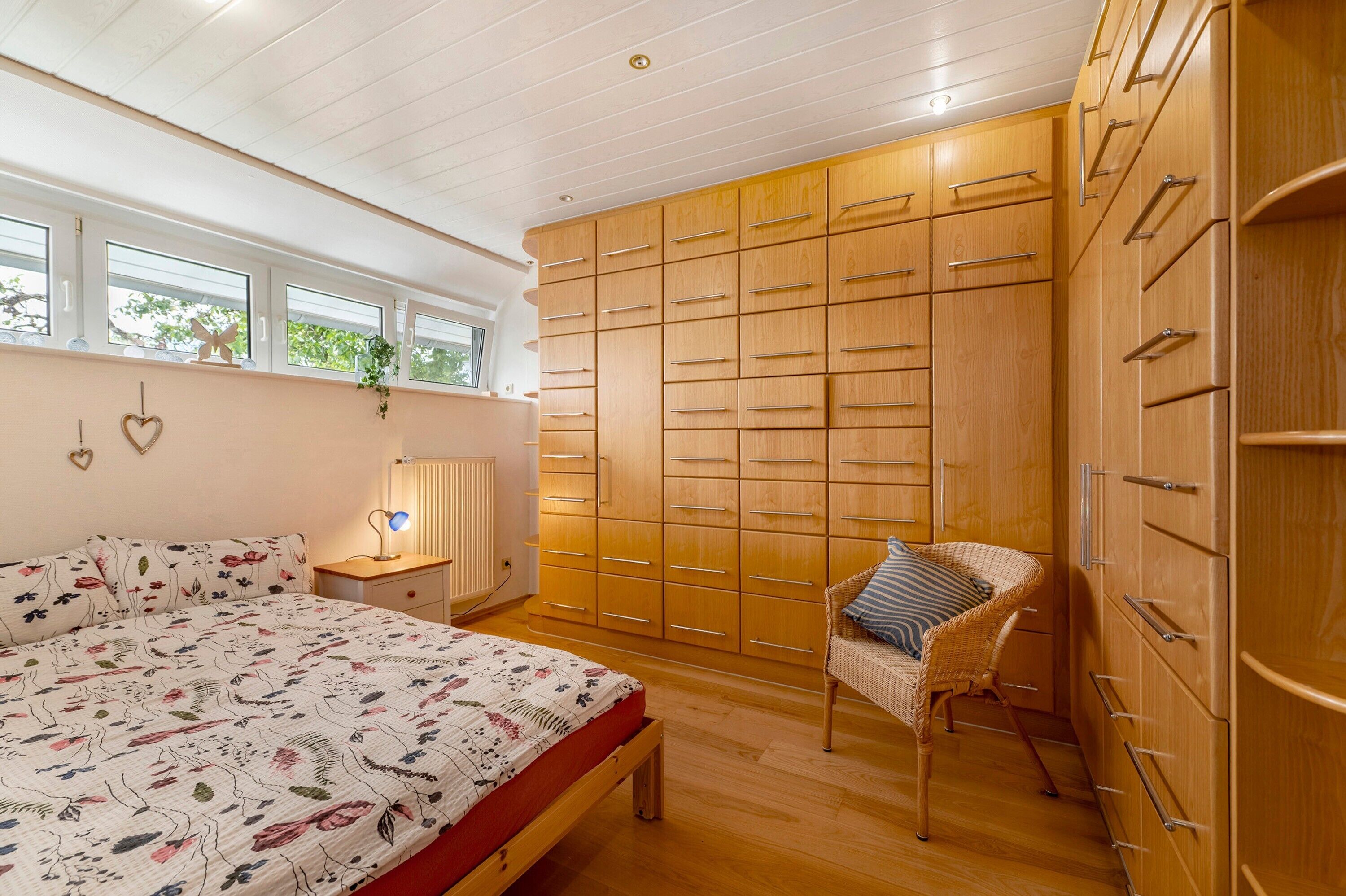 Ein Schlafzimmer mit einem Bett, einem Holzschrank, einem Sessel und einem Fenster.