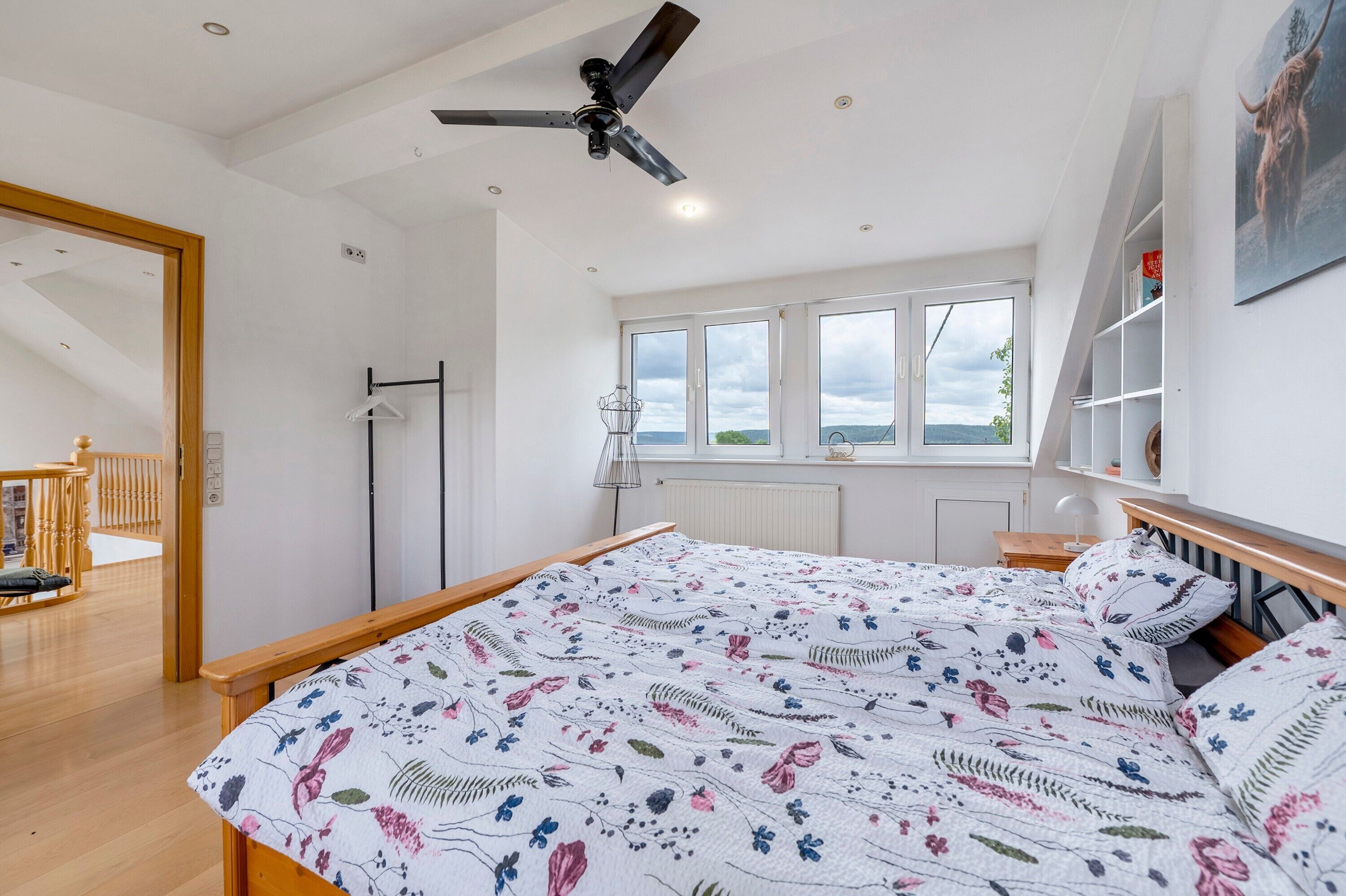 A bedroom with a bed, a ceiling fan, a radiator, and a window with a view.