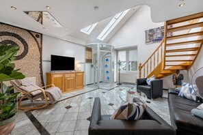 Uma sala de estar moderna com televisão, assentos, escada e porta de vidro que dá para outro cômodo.