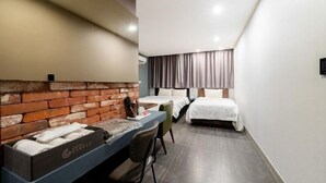 Hotellihuone, jossa on yksi seinä koristeltu tiilillä, työpöytä tuolilla, kaksi sänkyä ja ikkuna, jossa on verhot.