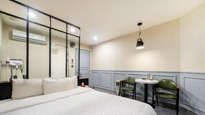 Hotellihuone, jossa on suuri sänky, pieni pöytä ja kaksi tuolia, peili ja ilmastointilaite.