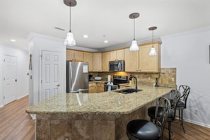 Una cocina con encimeras de granito, electrodomésticos de acero inoxidable, armarios de madera e iluminación colgante.