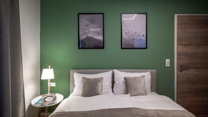 Habitación de hotel con cama, dos almohadas, mesita de noche con lámpara y dos cuadros en la pared.