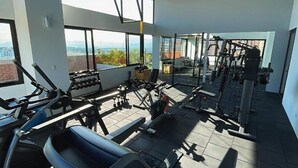 Un gimnasio con diferentes equipos de ejercicio, amplias ventanas y vistas de la ciudad.