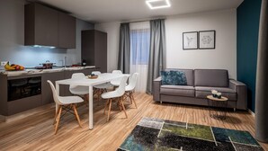A modern kitchen with white cabinets, a dining table with chairs, a grey sofa, and a small side table. - Family apartment in Schwaz (Schwaz)